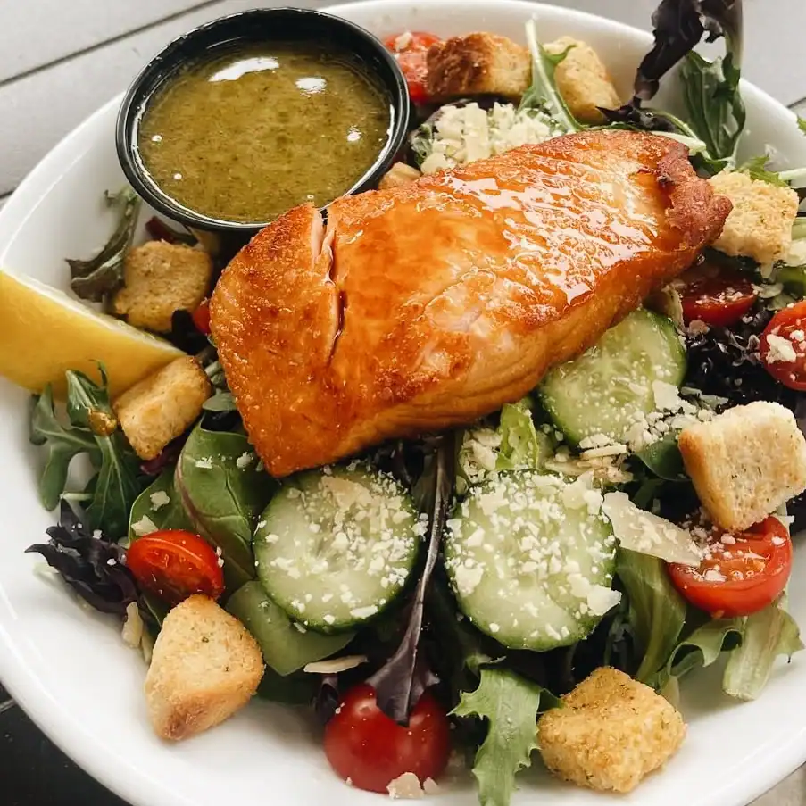 Pan Fried Salmon atop a mixed green fresh salad with dressing