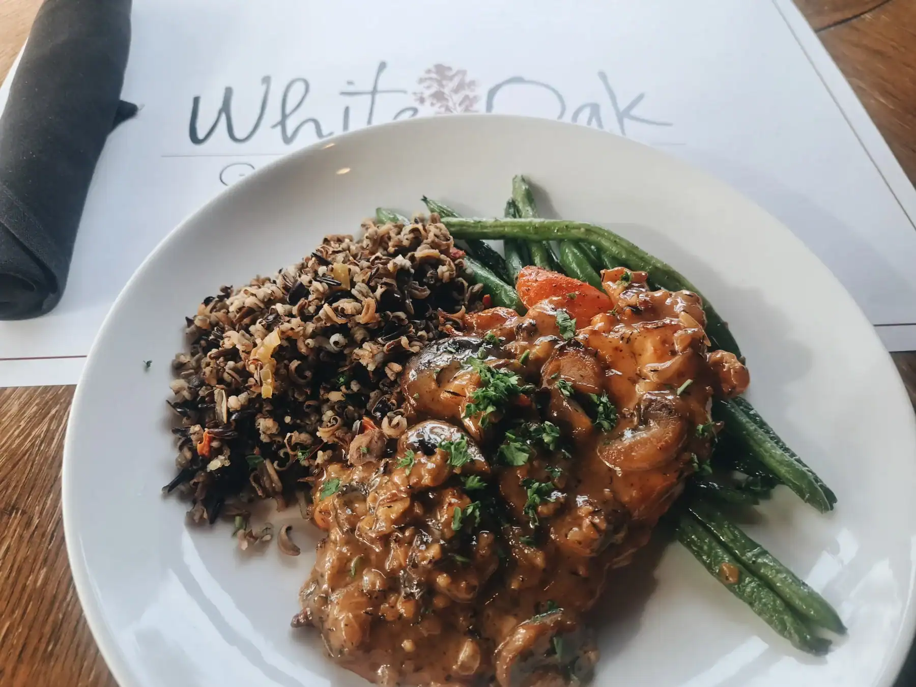 Dinner plate with main, wild rice and vegetable next to a napkin roll and placemat saying White Oak Grill