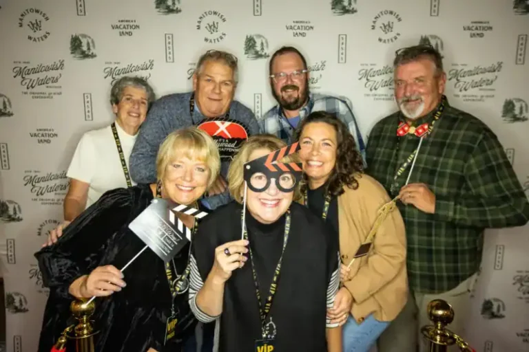 Group of men and women posing with props in a Photo Booth in front of a step and repeat at a private party celebrating the rebrand of the Manitowish Waters Visitors Bureau