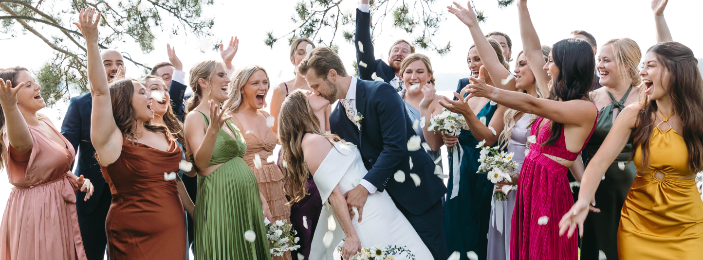 bride and groom kissing while surrounded by friends throwing rose petals up in the air after a lakeside ceremony at Chippewa Retreat Resort in Manitowish Waters, WI