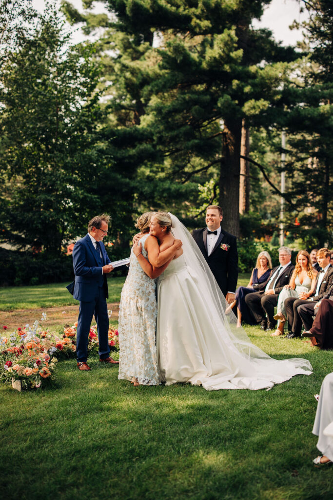 Bride hugs loved one before vow exchange during ceremony on Lakeside Lawn at Chippewa Retreat Resort