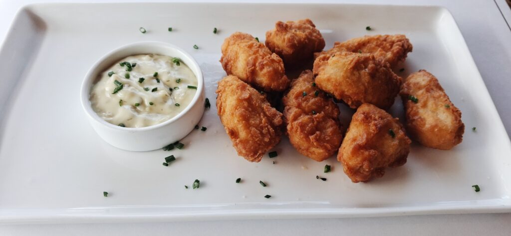 fried walleye bites plated on a white simple modern plate with a side bowl of tartar sauce and dusted with chives