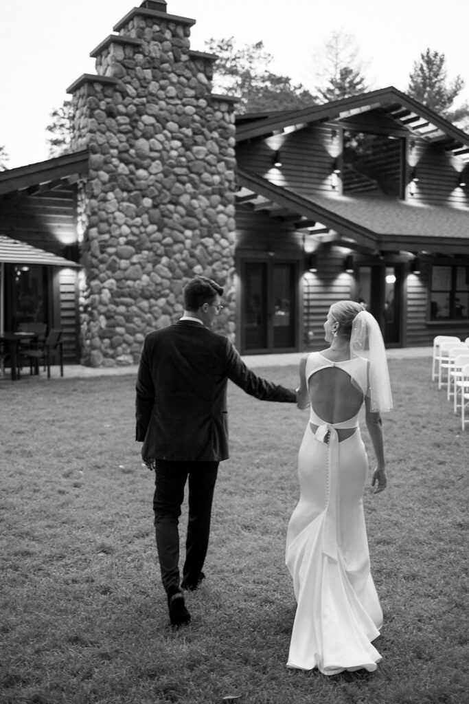 bride and groom walking up the lawn to a large northern Wisconsin lodge for their wedding reception