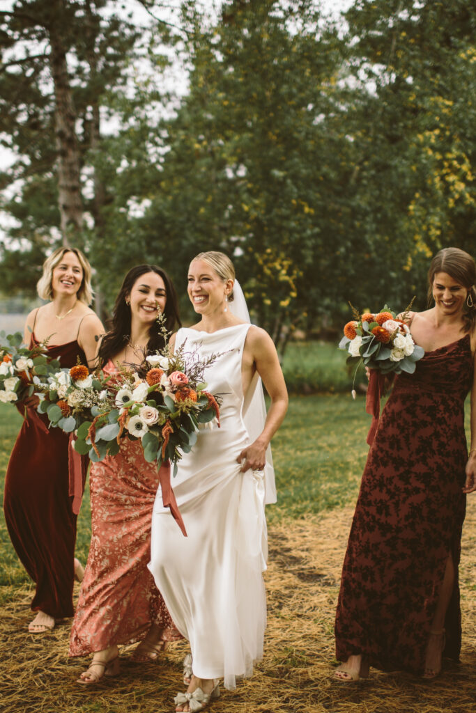 bride walking with her bridesmaids across a green lawn with brown pine needles for a fall lakeside wedding in the north woods of Wisconsin