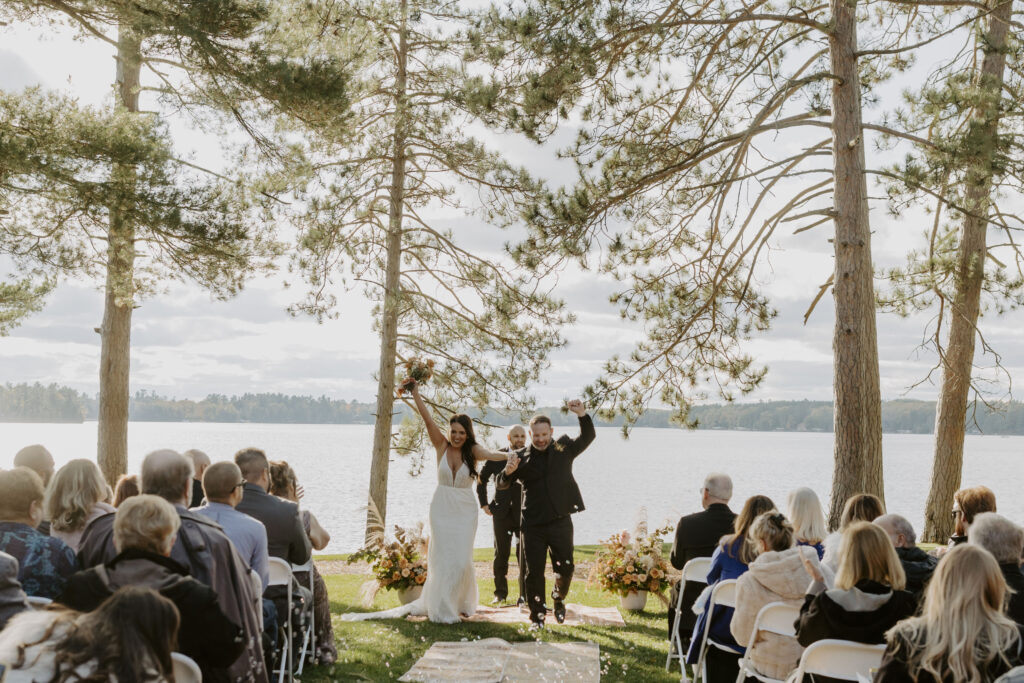 Bride and groom excited walking down aisle after vows overlooking lake with pine trees
