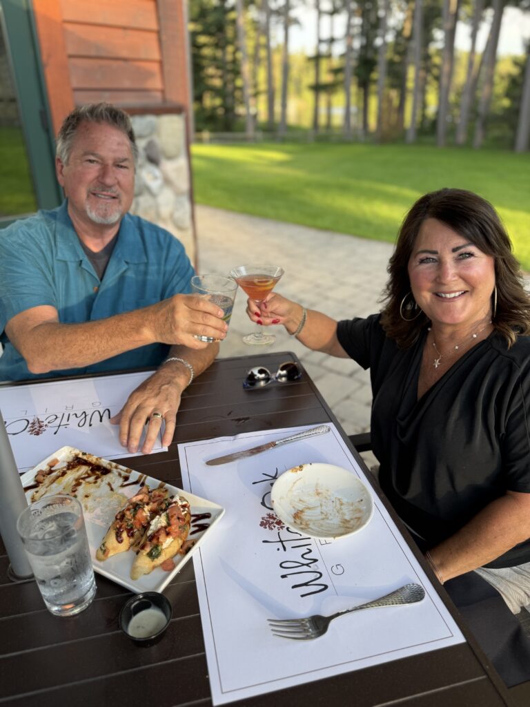 couple cheering glasses seated at a patio table at an outdoor restaurant