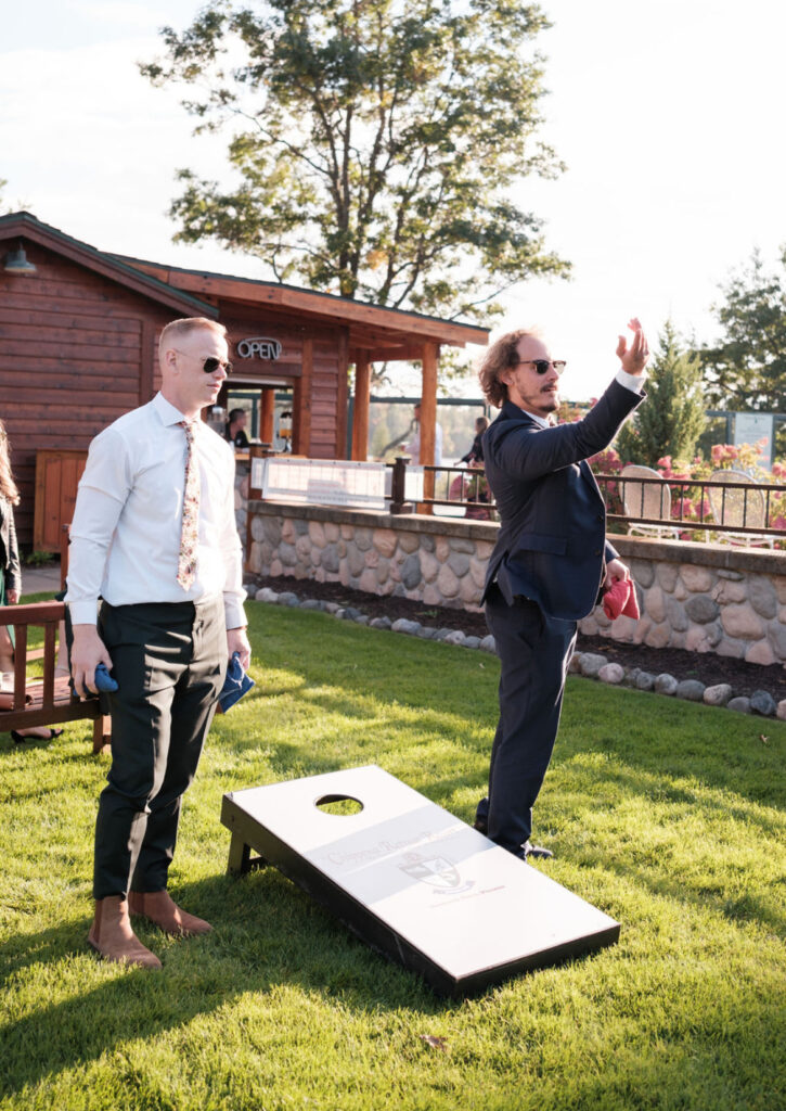 two men in suits playing corn hole on the lawn at Chippewa Retreat Resort in Manitowish Waters, Wi. The Swim Club pool and cabana are in the background.