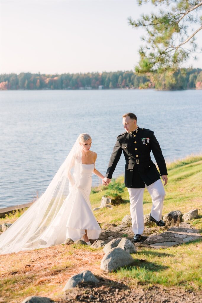 bride and groom walking up a grassy hill from the edge of lake Manitowish. Groom is in his formal marine attire and bride is in a white wedding dress with a veil. fall in Manitowish Waters, WI at Chippewa Retreat Resort
