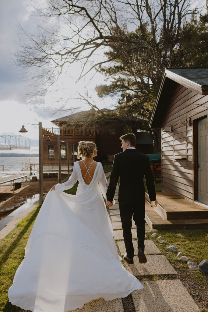 Bride and Groom Walking Down the Marina Path of square pavers with the lake and docks to the left of them, building and trees in the distance
